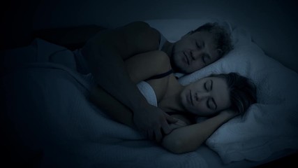 A beautiful young couple snuggle in bed at night in the dark