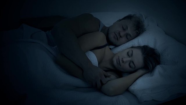 A beautiful young couple snuggle in bed at night in the dark