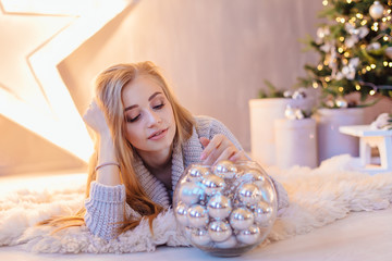 Beautiful young woman laying next to the big star with bowl full of silver balls in a holiday interior with Christmas tree