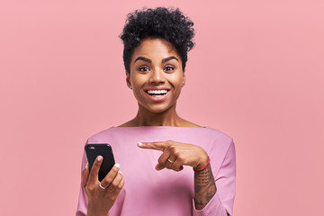 Cheerful African American female model checks in network on smartphone or read good news, indicates...