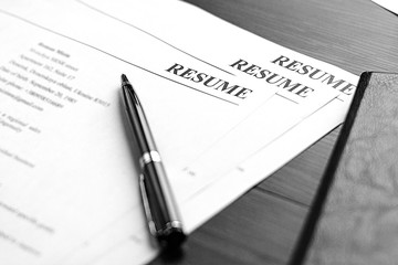 Resume (curriculum vitae, cv) and pen on a written wooden table. 