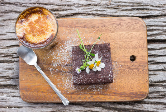 Daisy Flower on Chocolate Brownie Cake with Latte Coffee on Chopping Board on Wood Table Flatray