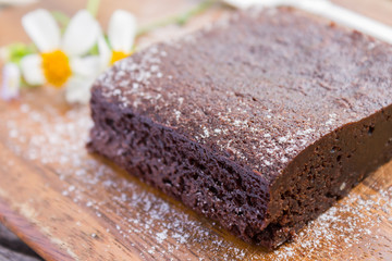 Chocolate Brownie Cake and Daisy Flower on Chopping Board on Wood Table Close Up