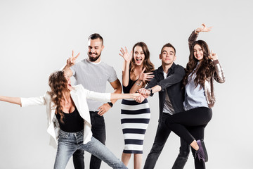 Company of  girls and guys dressed in stylish casual clothes are fooling around on a white...