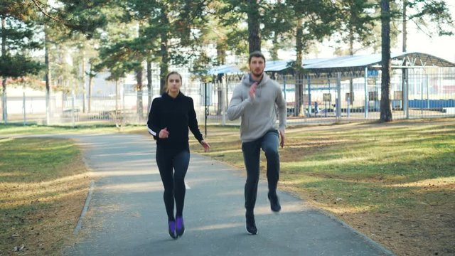 Beautiful couple pretty girl and bearded guy are exercising in park together running and jumping. Active lifestyle, healthy youth and leisure concept.