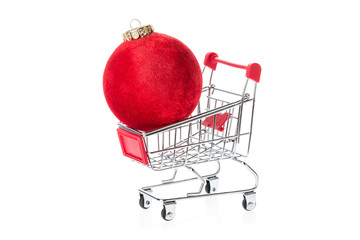 Shopping trolley with red christmas ball isolated on white background. Christmas expenses and shopping concept.