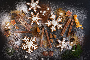 Christmas or New Year background of Gingerbread cookies, spices, nuts with sugar and snowflakes. Top view on dark stone background