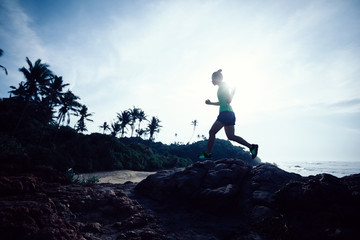 Obraz premium Woman trail runner running at rocky mountain top on seaside
