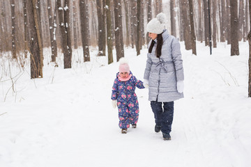 Family, winter and nature concept - Young cheerful mother with cute little daughter walking in the snow park