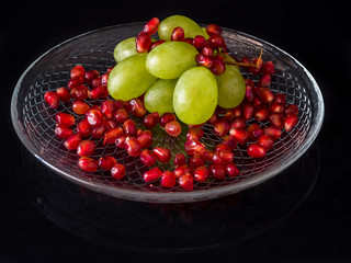 Pile of pomegranate and grapes on glass plate with black background. Simple fruits on black background.