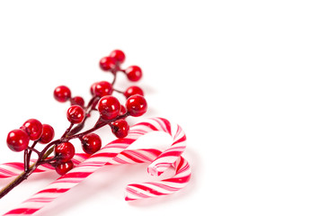 Two Christmas candy canes with a branch of decorative berries on white background isolated.