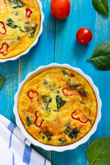 Frittata with fresh vegetables and spinach. Italian omelet in ceramic forms on a blue wooden background. Top view.