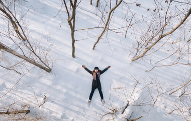 A pretty girl in a coat lies on the snow, spreading her arms and legs. Feel free. Top view. Drone.