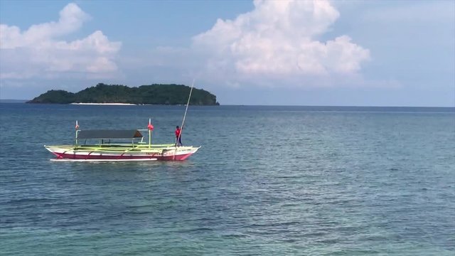 Boat operator poling through shallow water off of Agta Beach on Biliran Island, Philippines, with Dalutan Island in the background.