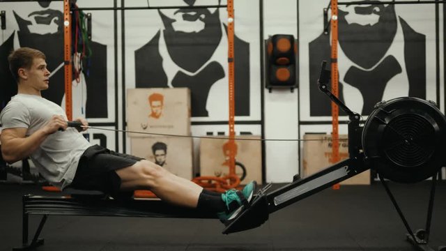 Fitness young man using rowing machine in the gym crossfit training at night student professional athlete bodybuilder