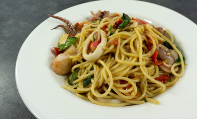 Spaghetti seafood in a white dish on a black stone floor table.