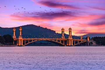 Fototapeta premium Illuminated bridge over the river, twilight, evening view on Putra lake. Amazing sunset sky over the city, Putrajaya, Malaysia.