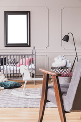 Vertical view of vintage grey armchair in trendy mid century baby room interior with mockup in black frame on the empty grey wall