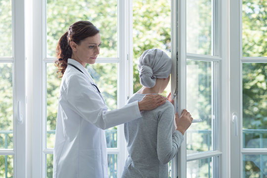 Friendly doctor in white uniform supporting sick girl with headscarf
