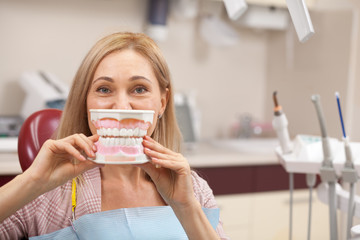Happy mature female patient smiling posing with a big dentures mold in front of her mouth. Cheerful...