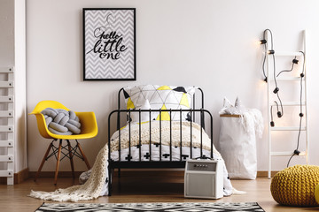 Stylish yellow chair with grey knit pillow next to metal bed in black and white bedroom for kid © Photographee.eu