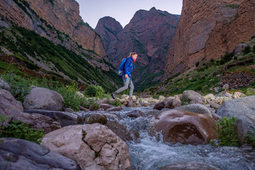 Girl with a backpack crosses the river in the mountains.