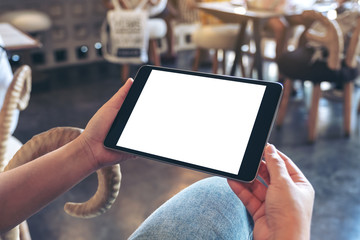 Mockup image of a woman holding black tablet pc with blank white screen horizontally while sitting in cafe