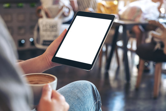Mockup image of woman's hands holding black tablet pc with blank screen while drinking coffee in cafe