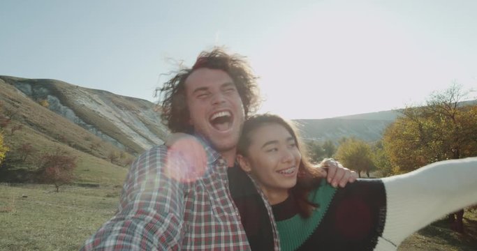 Beautiful multicultural couple have a good time together at nature , they taking video selfies with camera , smiling and making funny faces.