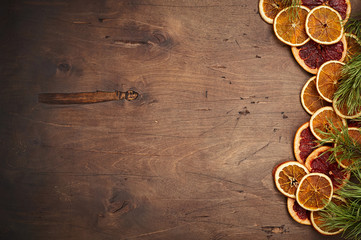 Fototapeta na wymiar Dark brown vintage rustic wooden background with fir branches, dried orange and grapefruit rings