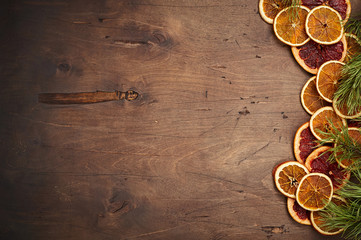 Dark brown vintage rustic wooden background with fir branches, dried orange and grapefruit rings