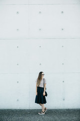 Beautiful fashionable girl in a skirt and with a bag goes along the wall.