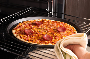 Woman taking out ready pizza out of the oven.