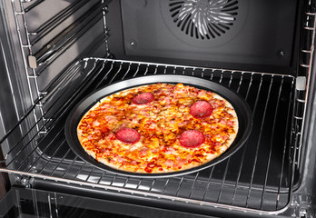 Cooking homemade pizza with salami sausage in oven.