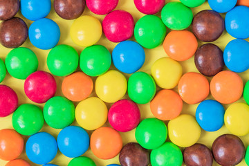 Colorful Background of multicolored sweet candies. Round bonbons scattered on yellow background