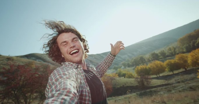 A cute curly hair guy with a large smile, have trip , he taking some selfie video of himself and showing the amazing landscape from around.