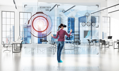 Girl in office interior in virtual reality mask using innovative technologies. Mixed media