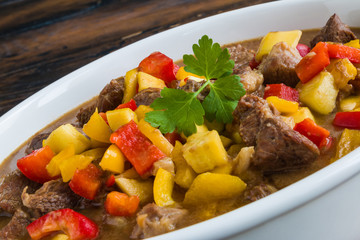 Beef stew with vegetables, bell peppers, zucchini, garlic, dark beer and spices in white casserole, close-up