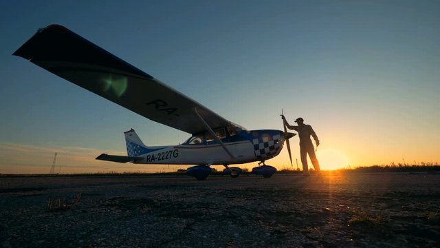 Male aviator cleaning a plane on a sunset background, side view.
