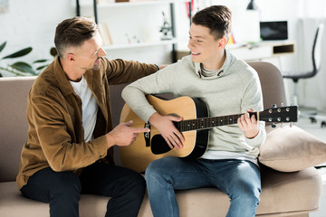 smiling teen son playing acoustic guitar for father at home