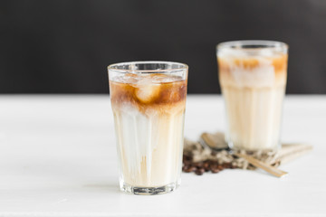Ice coffee in a glass with cream over and coffee beans on the table