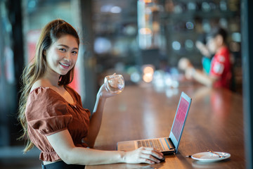 Beautiful Attractive Business Asian woman working with laptop holding coffee and looking in monitor smile and have positive emotional feeling so happiness,Business Startup Concept