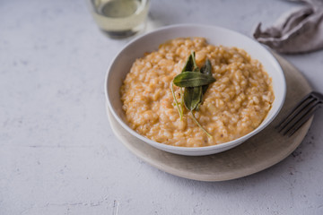 Pumpkin risotto with parmesan and sage served with a glass of white wine. Side view, concrete background