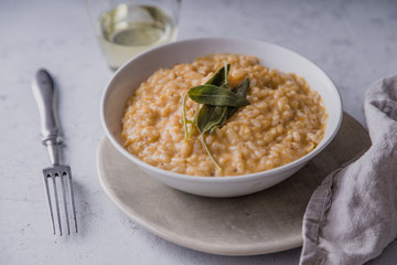 Pumpkin risotto with parmesan and sage served with a glass of white wine. Side view, concrete background