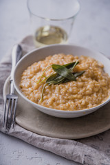 Pumpkin risotto with parmesan and sage served with a glass of white wine. Side view, concrete background