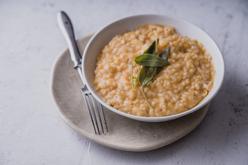 Pumpkin risotto with parmesan and sage served with a glass of white wine. Side view, concrete background