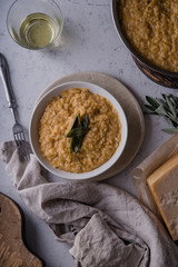 Pumpkin risotto with parmesan and sage served with a glass of white wine. Overhead view, concrete background