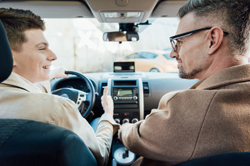 back view of handsome father and smiling teen son looking at each other in car