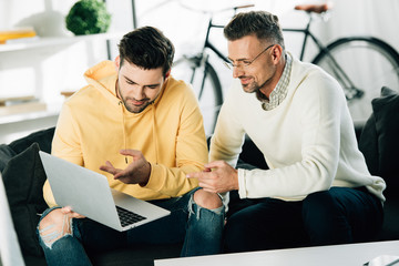 son showing something on laptop to mature father on sofa at home