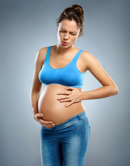 Pregnant woman suffers from abdominal pain on gray background. Medical concept